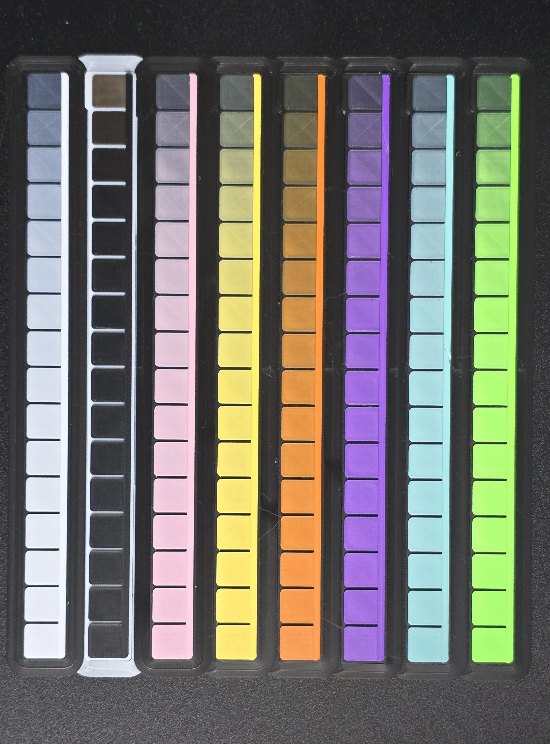 Eight printed HD wedges with stepped patches beside opaque reference rails, ordered white, black, pink, yellow, orange, purple, cyan, and green from left to right.